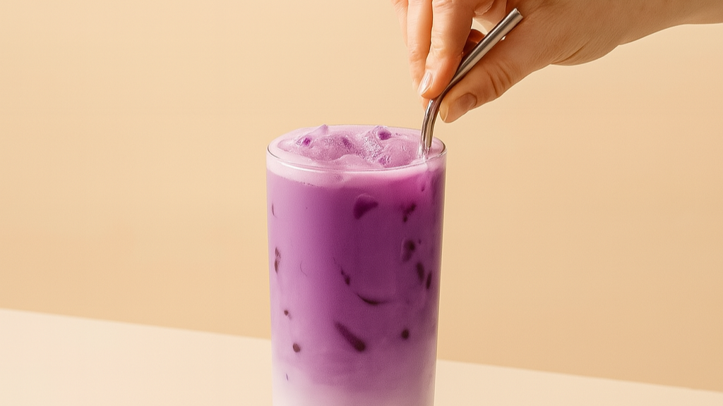ube latte dans un verre avec des glaçons et une paille metalique siroté